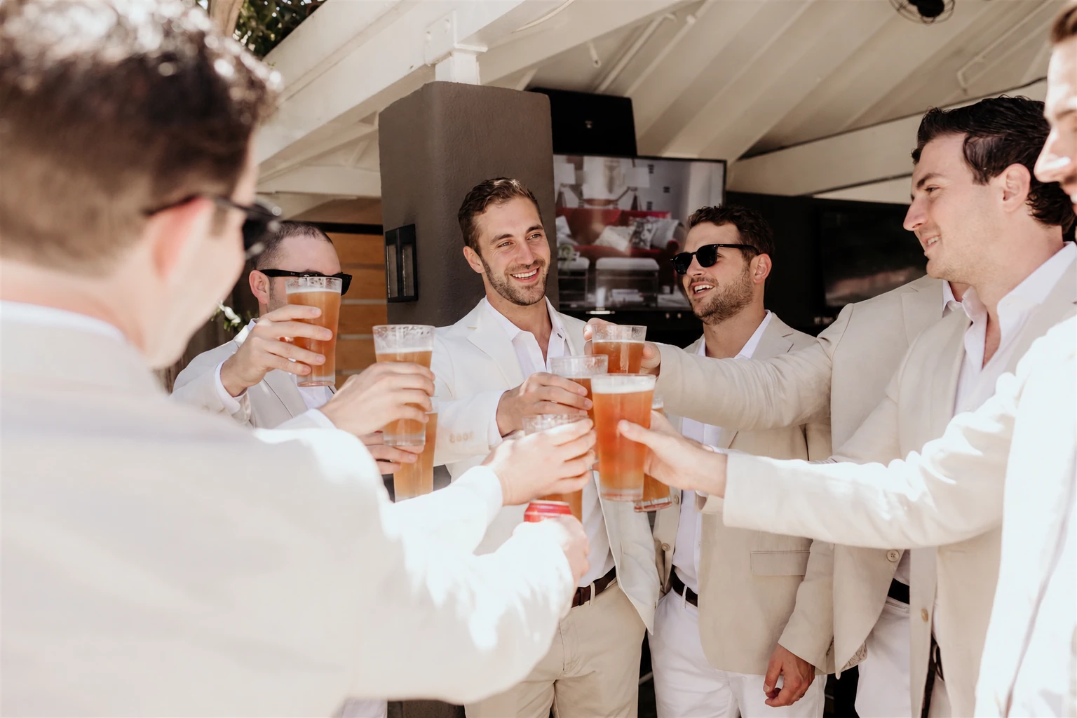 A stylish group of men in light suits raising drinks together