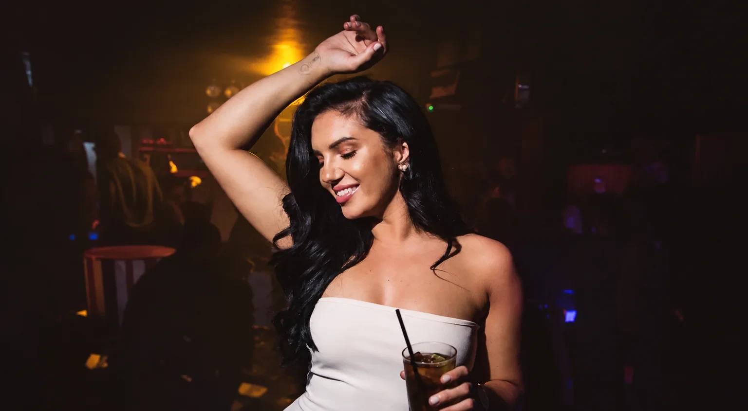 A woman dancing with a cocktail in a warmly lit nightclub